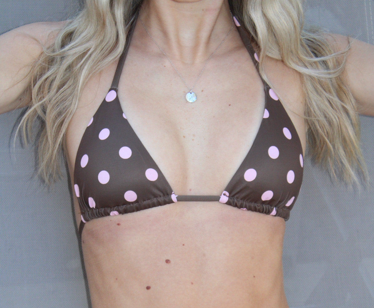 Person wearing a brown bikini top with pink polka dots against a neutral background